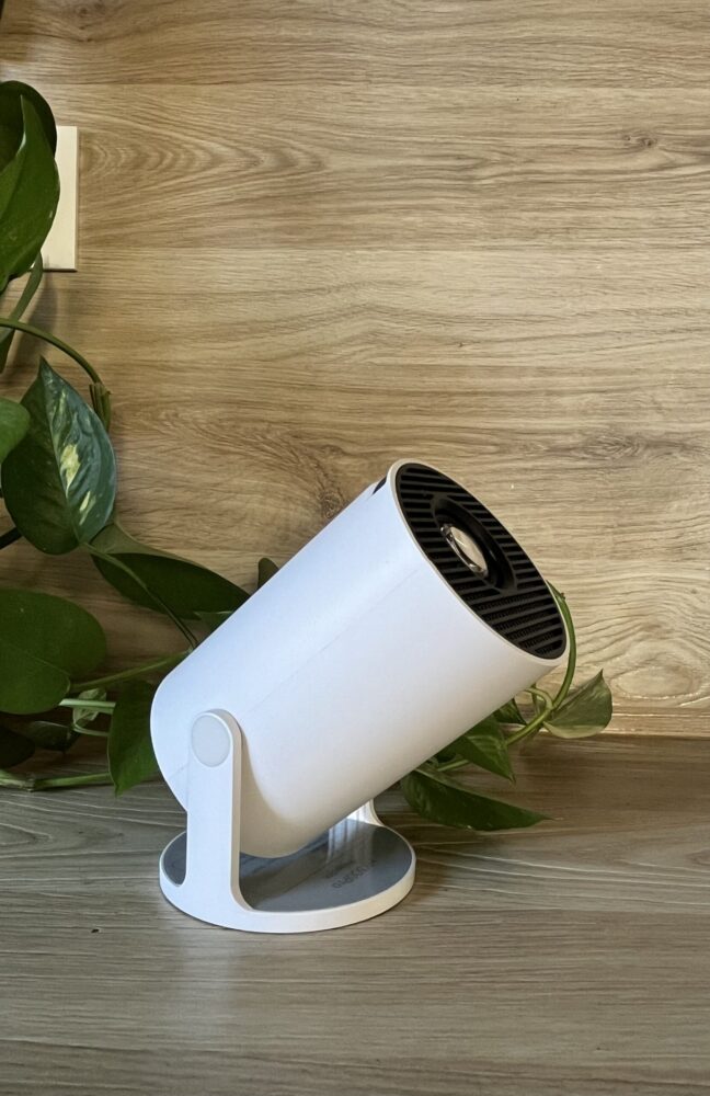 Projecteur d’ambiance Planète Lumi – Design épuré et naturel Projecteur d’ambiance Planète Lumi blanc posé sur une surface en bois clair, entouré de feuilles vertes, illustrant un design minimaliste et naturel.